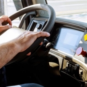 Foto horizontal colorisda mostra mãos masculinas em um volante com painel de caminhão